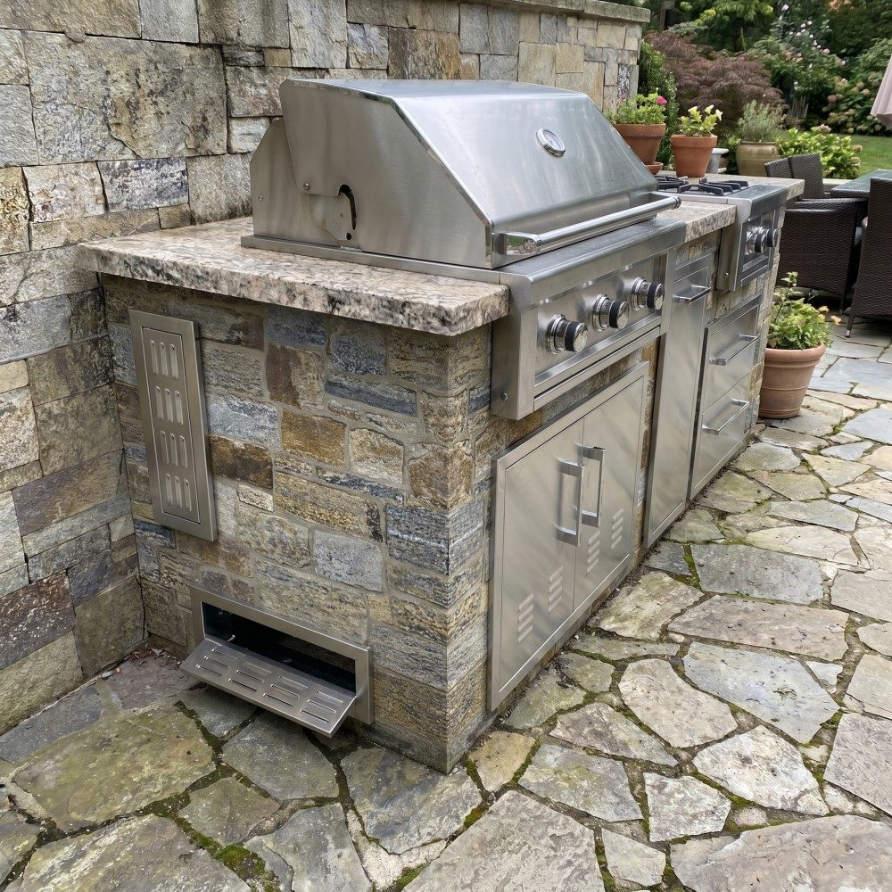Stone grill island: Built-in grill island with side vent and storage in natural stone.